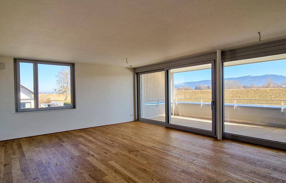Helles, leeres Wohnzimmer mit Holzboden und weitem Blick auf die Landschaft.
