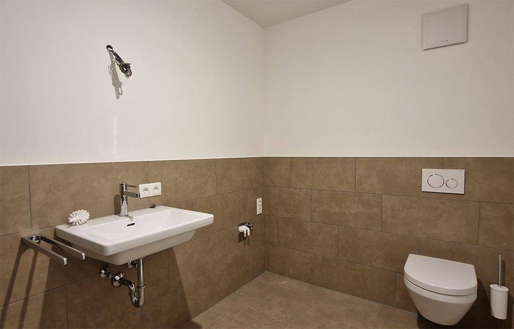 Einfaches Gäste-WC mit Wand-WC, Waschbecken und beigen Fliesen.