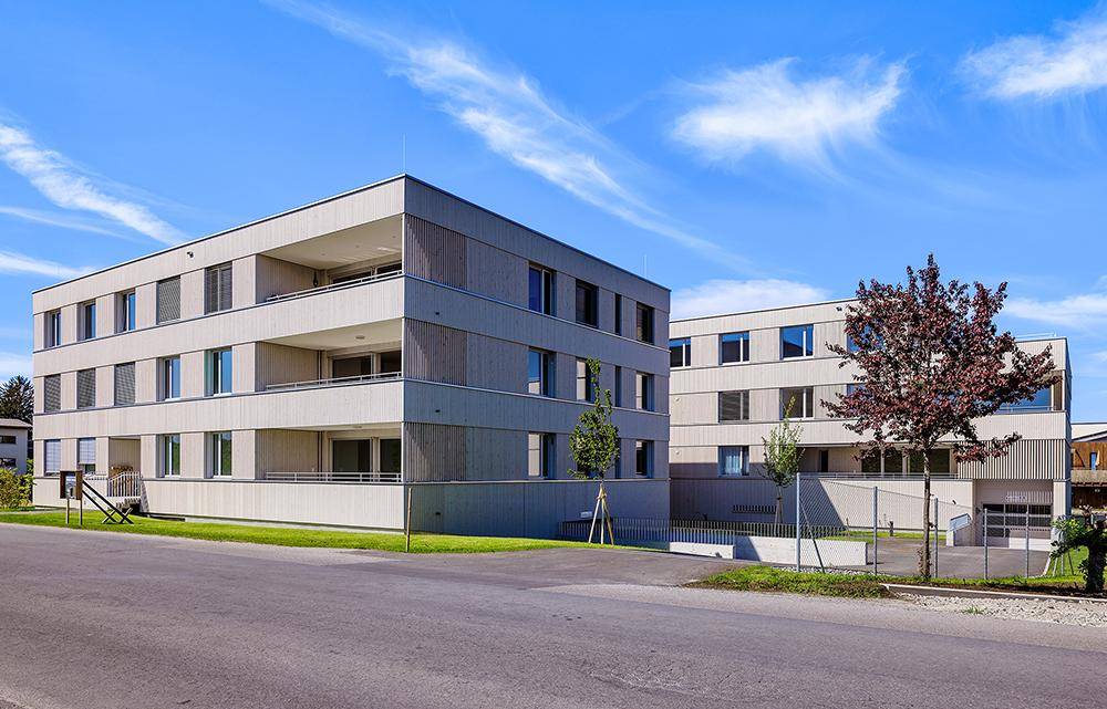 Moderne Wohngebäude mit heller Holzfassade und Balkonen unter blauem Himmel.