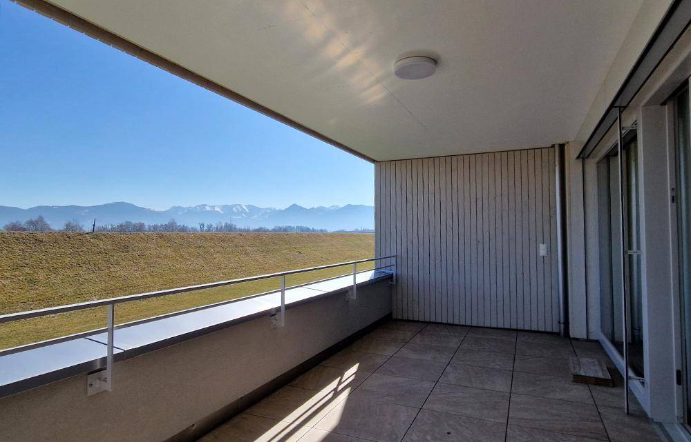 Großer, leerer Balkon mit Fliesenboden und weitem Blick auf die Berge und Felder.