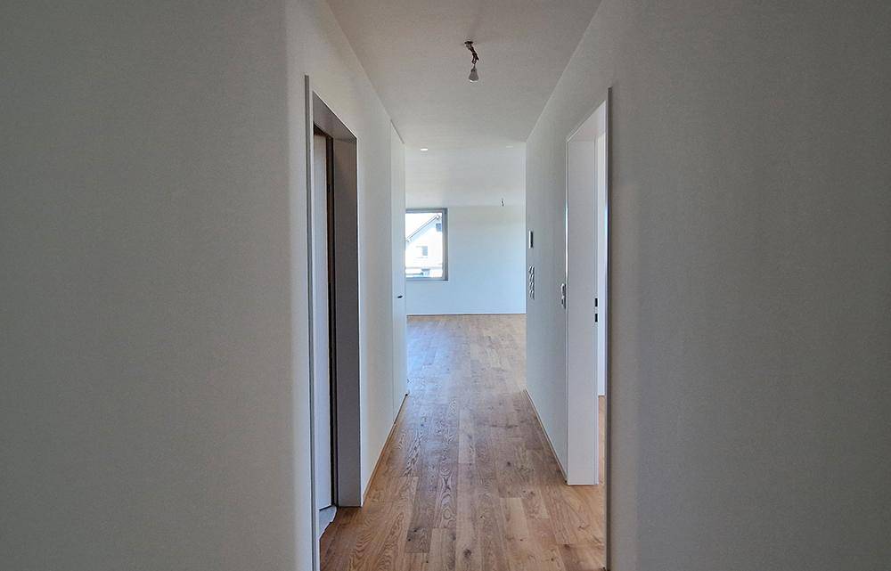 Heller Flur mit Holzboden und weißen Wänden, der zu weiteren Räumen führt.