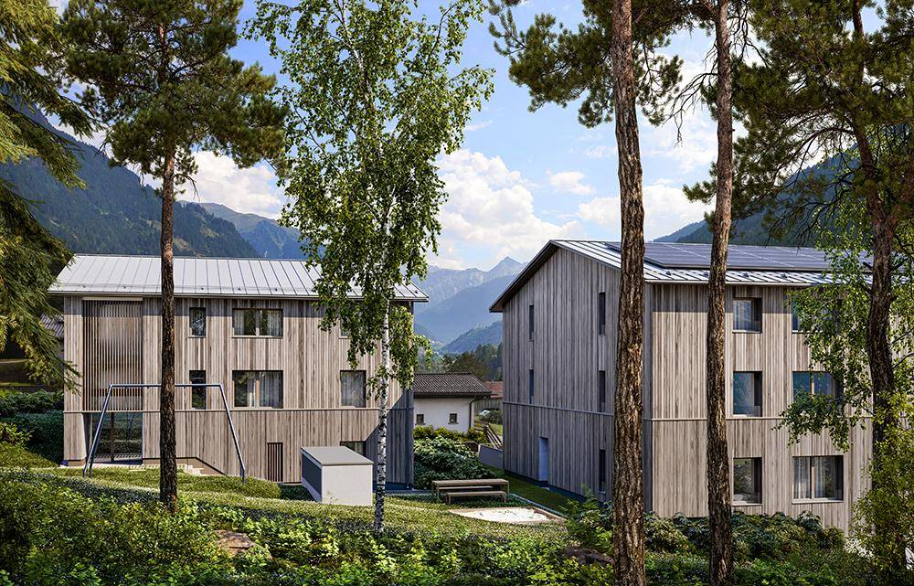Rückseite zweier moderner Gebäude mit Holzfassaden, umgeben von Bäumen und Bergblick.