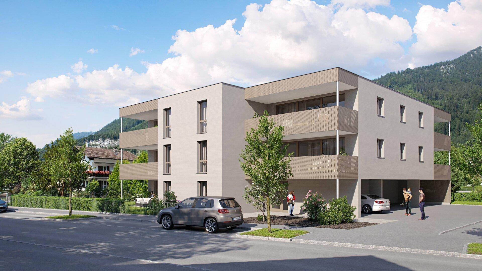 Ansicht eines modernen Mehrfamilienhauses mit Balkonen, Tiefgaragenzufahrt und Bergkulisse.