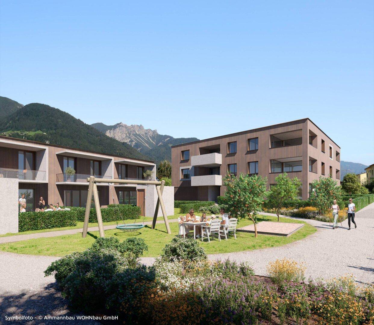 Moderne Wohngebäude mit Spielplatz und Grünflächen, umgeben von einer malerischen Berglandschaft.