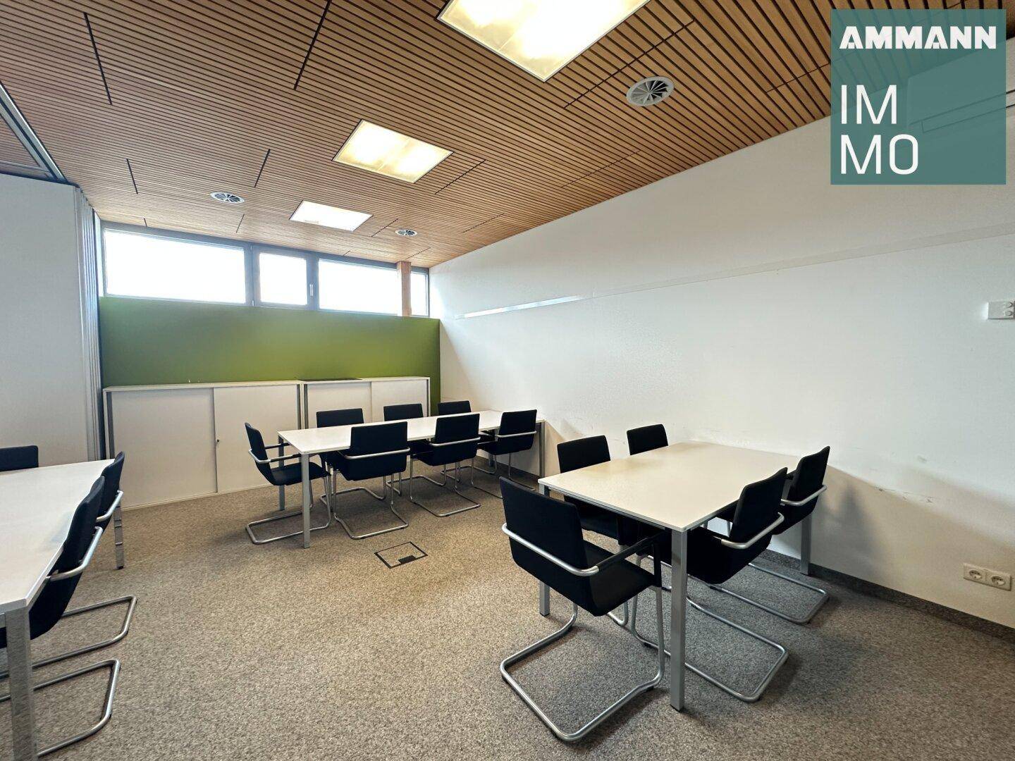 Konferenzraum mit mehreren Tischen und Stühlen, Holzdeckenverkleidung und Teppichboden.