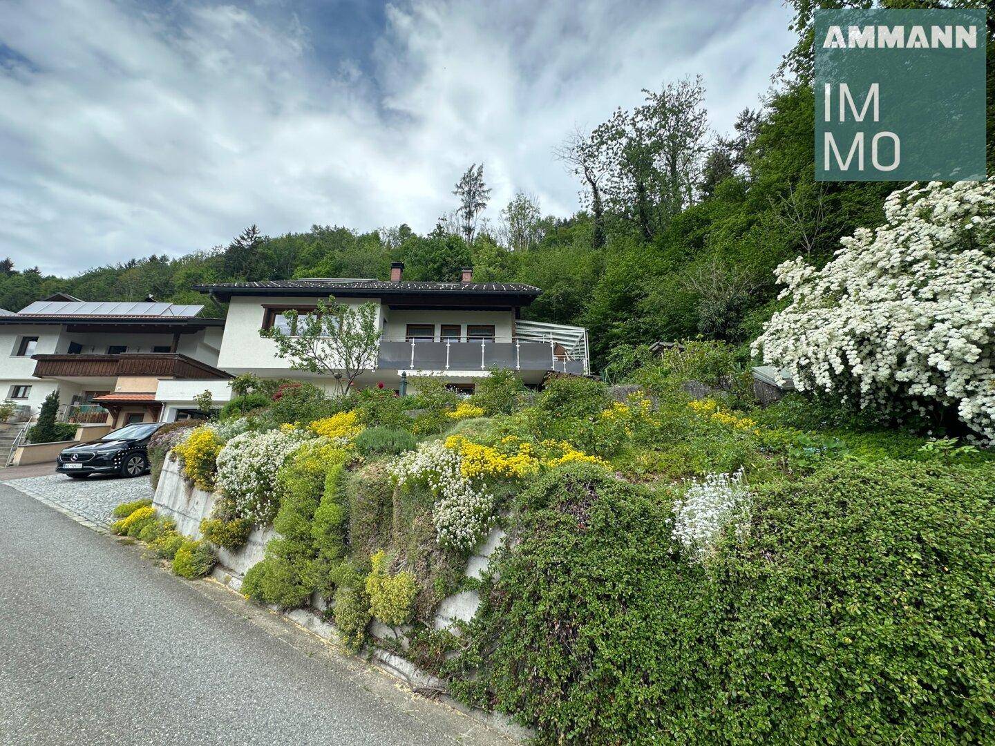 Ansicht des Hauses von der Straße mit üppiger Bepflanzung und einem Balkon.