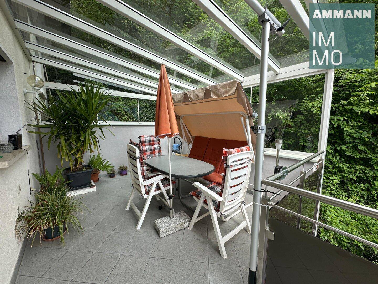 Überdachter Balkon mit Glasdach, Gartenmöbeln und Blick ins Grüne.