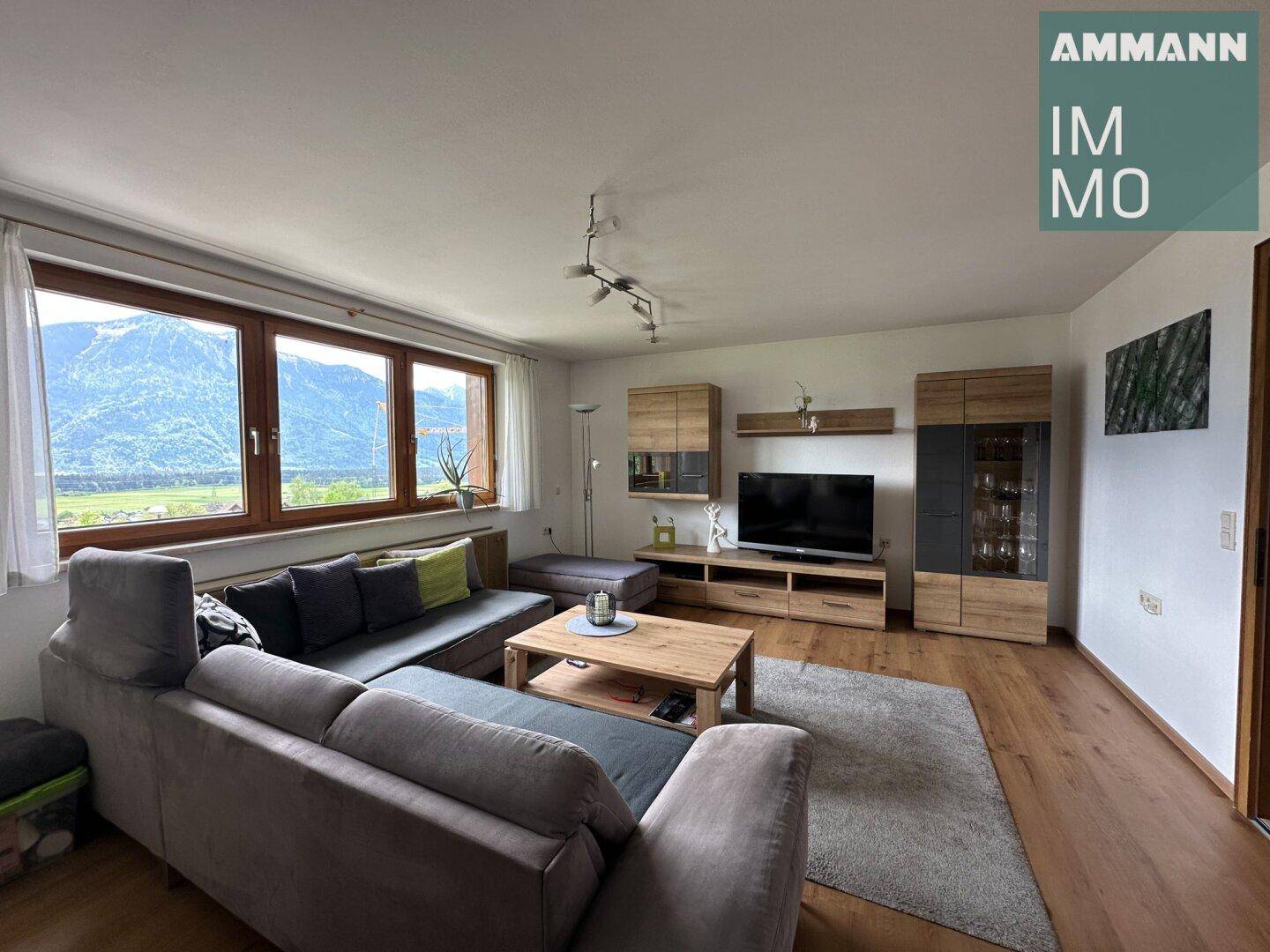Geräumiges Wohnzimmer mit großem Fenster, Holzboden und Blick auf die Berge.