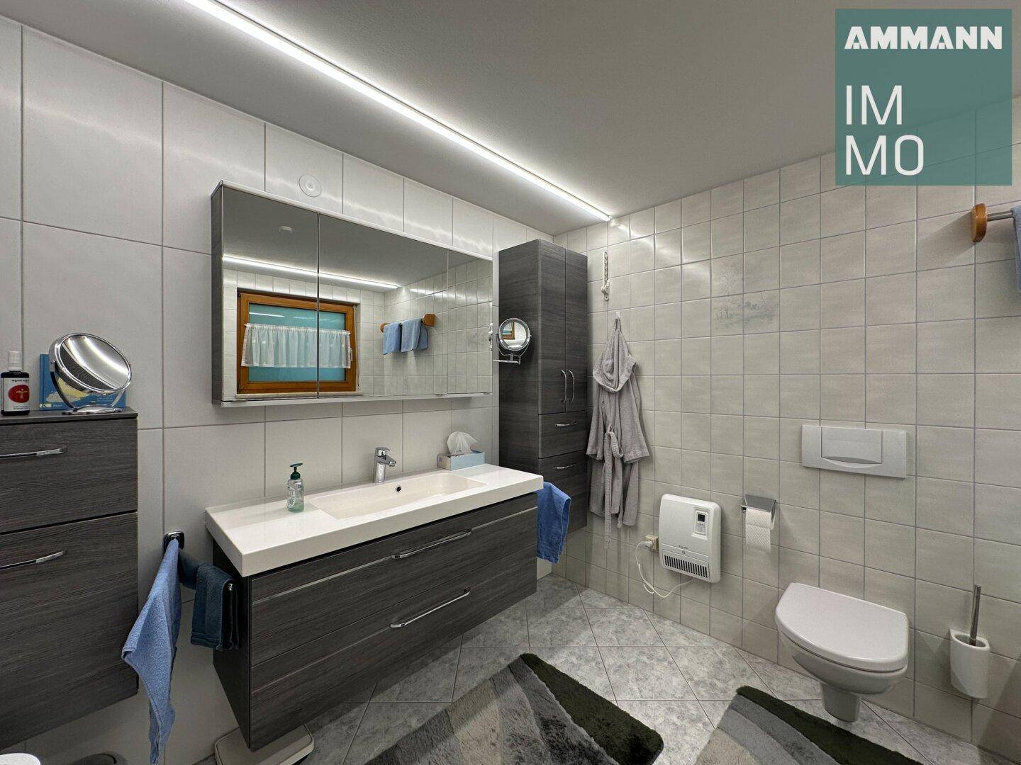 Modern gefliestes Badezimmer mit Waschtisch, Spiegelschrank und Wand-WC.