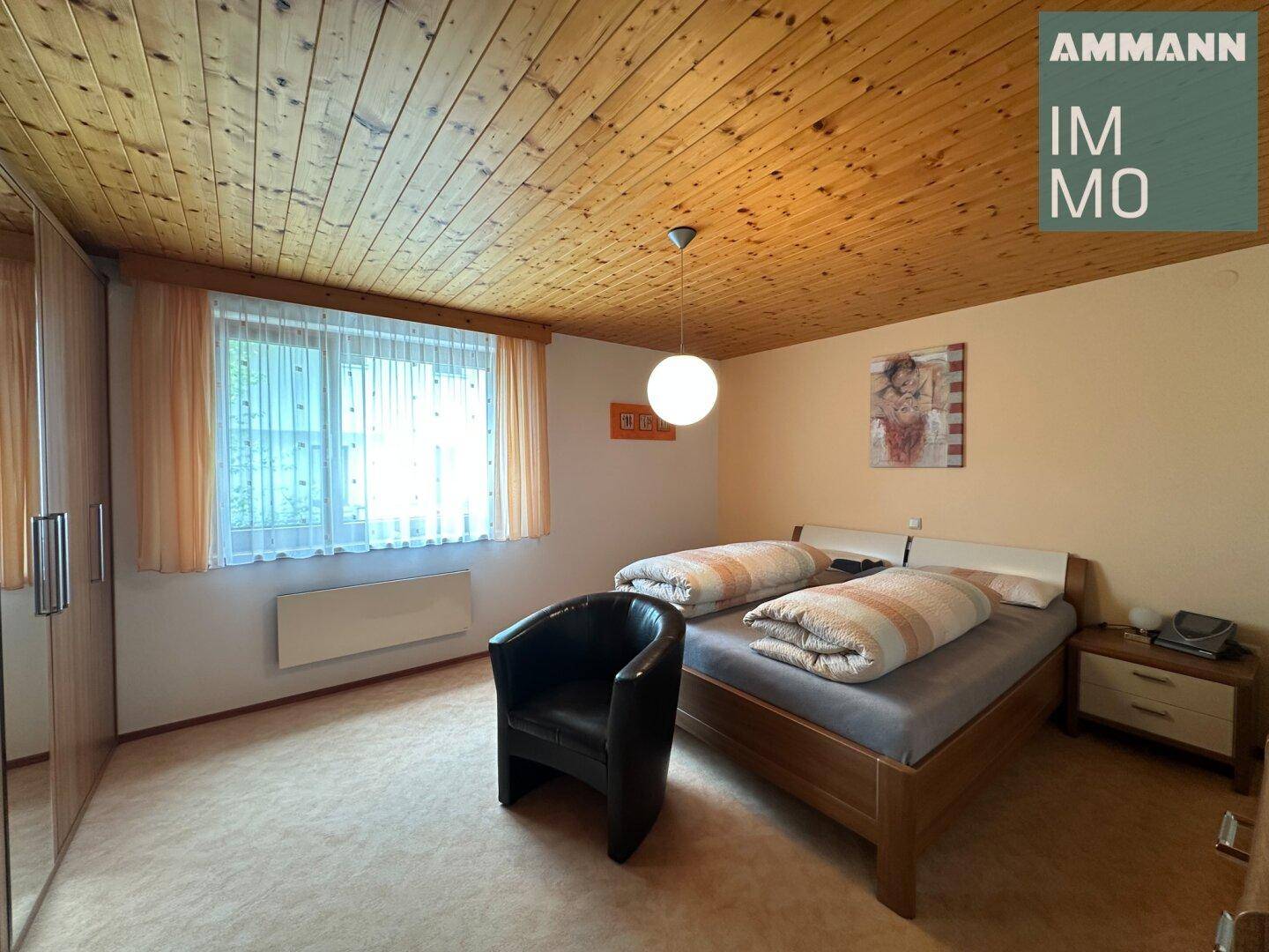 Gemütliches Schlafzimmer mit Holzdecke, Teppichboden und großem Fenster.