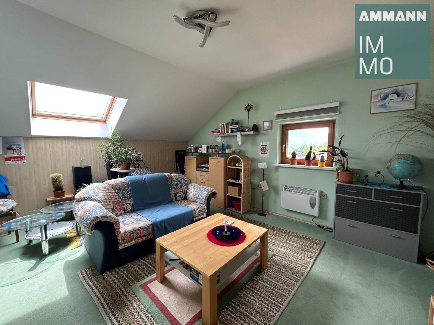 Helles Dachgeschoss-Wohnzimmer mit Dachfenster, gemütlicher Couch und Teppichboden.