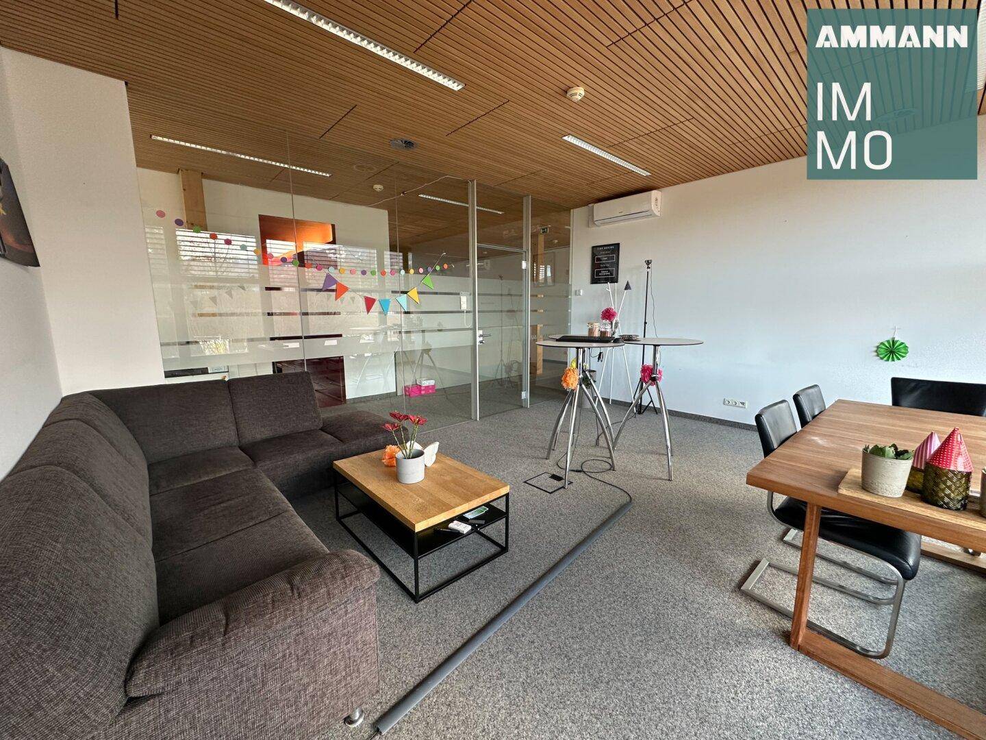 Geräumiger Loungebereich mit bequemer Couch, Holztisch und eleganten Glastrennwänden.