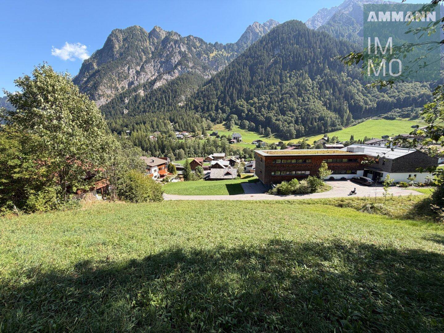 Sonniger Ausblick auf die alpine Landschaft mit bewaldeten Bergen und einem kleinen Dorf im Tal.