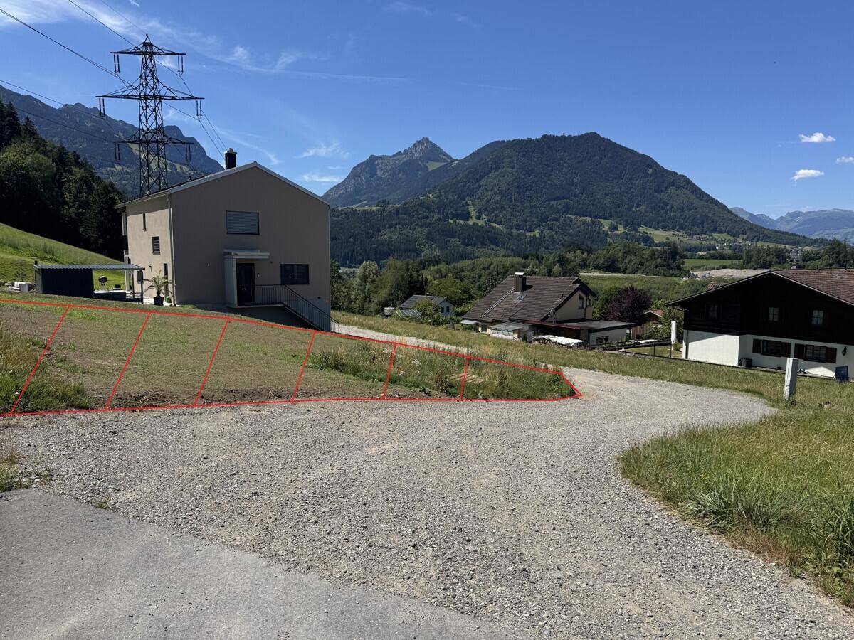 Grundstück mit Schotterweg und Blick auf die Berge sowie angrenzende Wohnhäuser in ländlicher Umgebung.