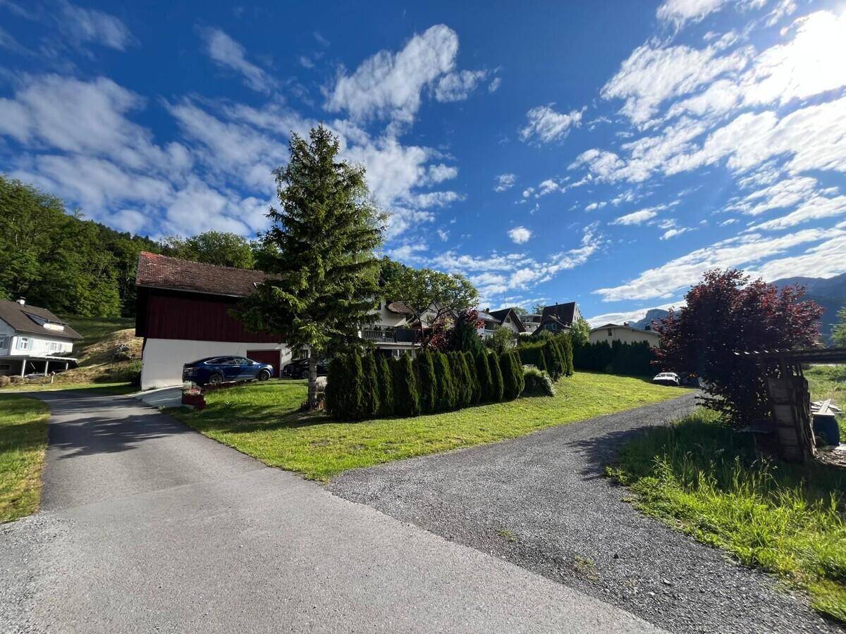 Weitläufige Auffahrt zum Haus, umgeben von grüner Landschaft und Bäumen unter bewölktem Himmel.