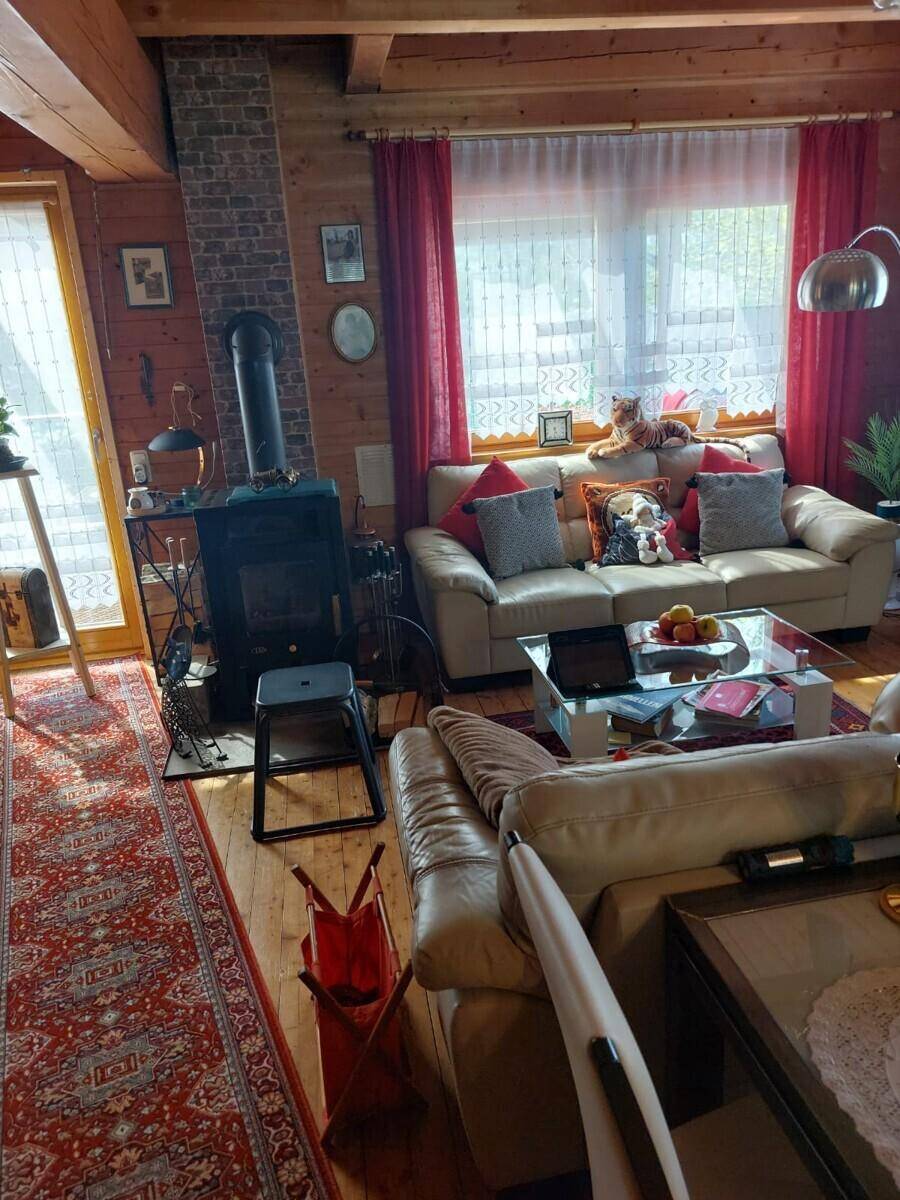 Rustikales Wohnzimmer mit Holzwänden, bequemen Sofas, Kaminofen und großem Fenster für viel Licht.