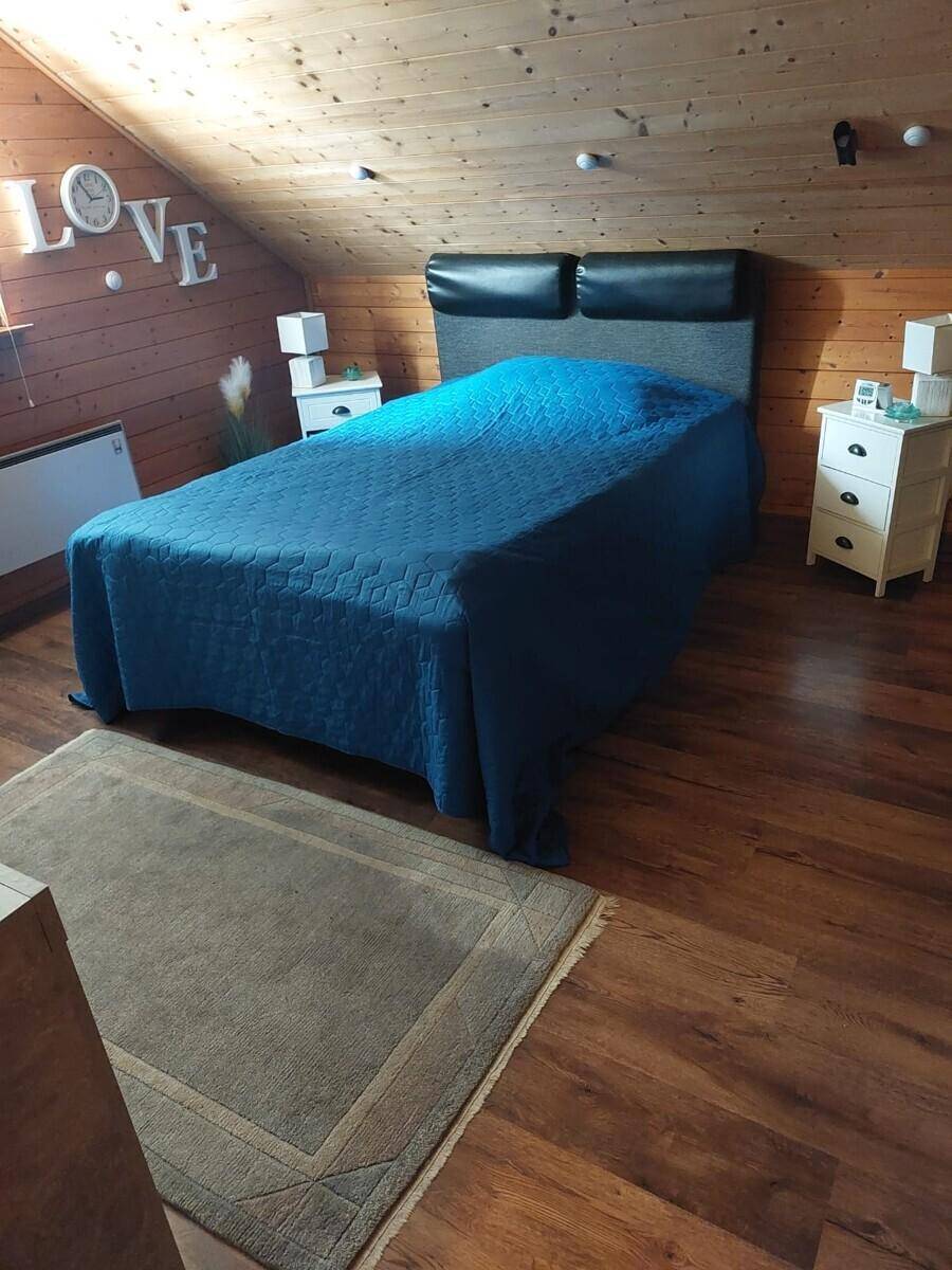 Schlafzimmer mit schräger Holzdecke, Holzboden, Doppelbett und Nachttischen in gemütlicher Atmosphäre.