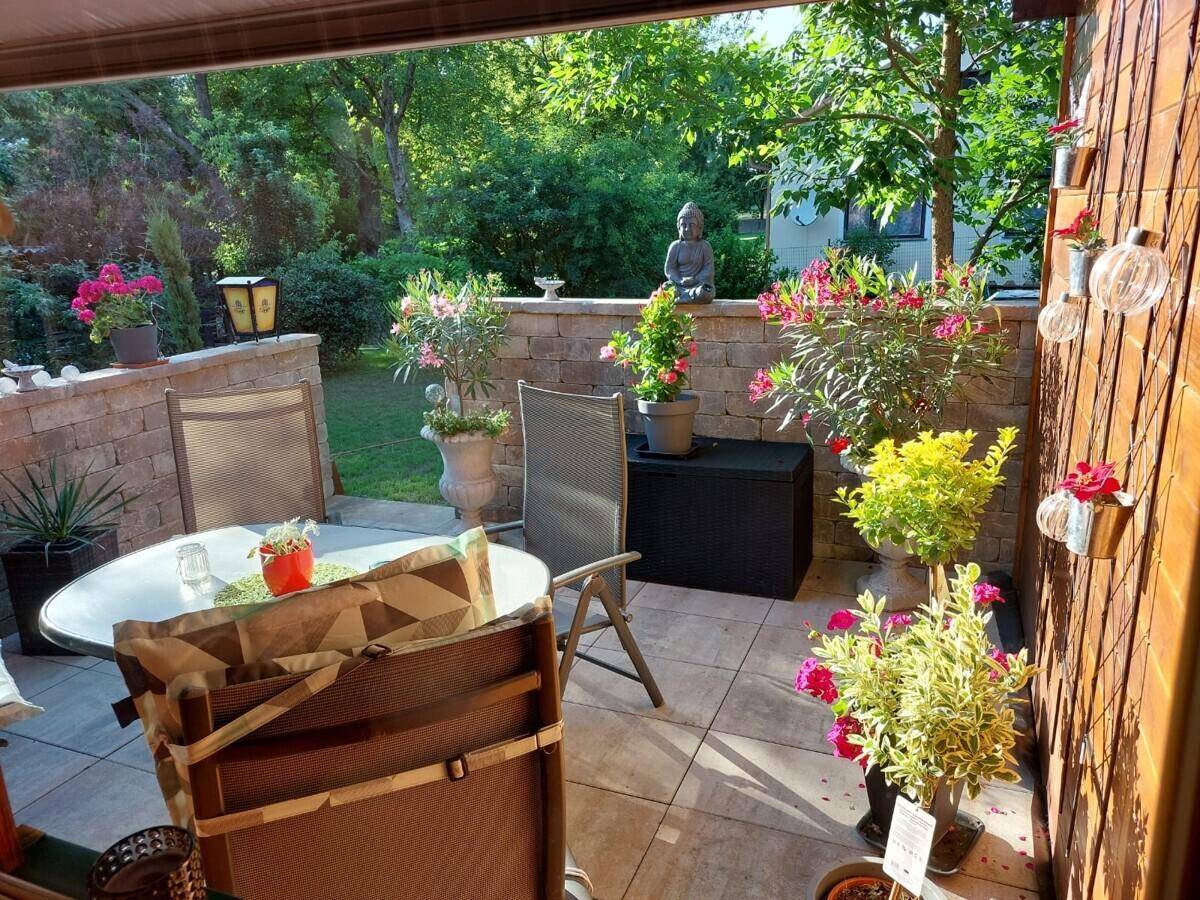 Gemütlicher, möblierter Sitzbereich auf einer gepflasterten Terrasse, umgeben von blühenden Pflanzen.