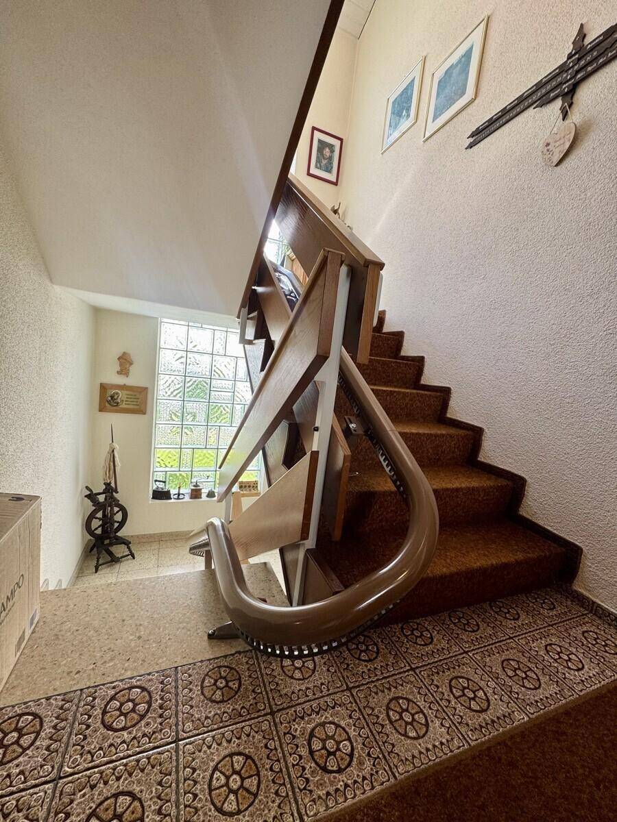 Treppenhaus mit Holzgeländer, Teppichstufen und dekorativen Bodenfliesen im Eingangsbereich.