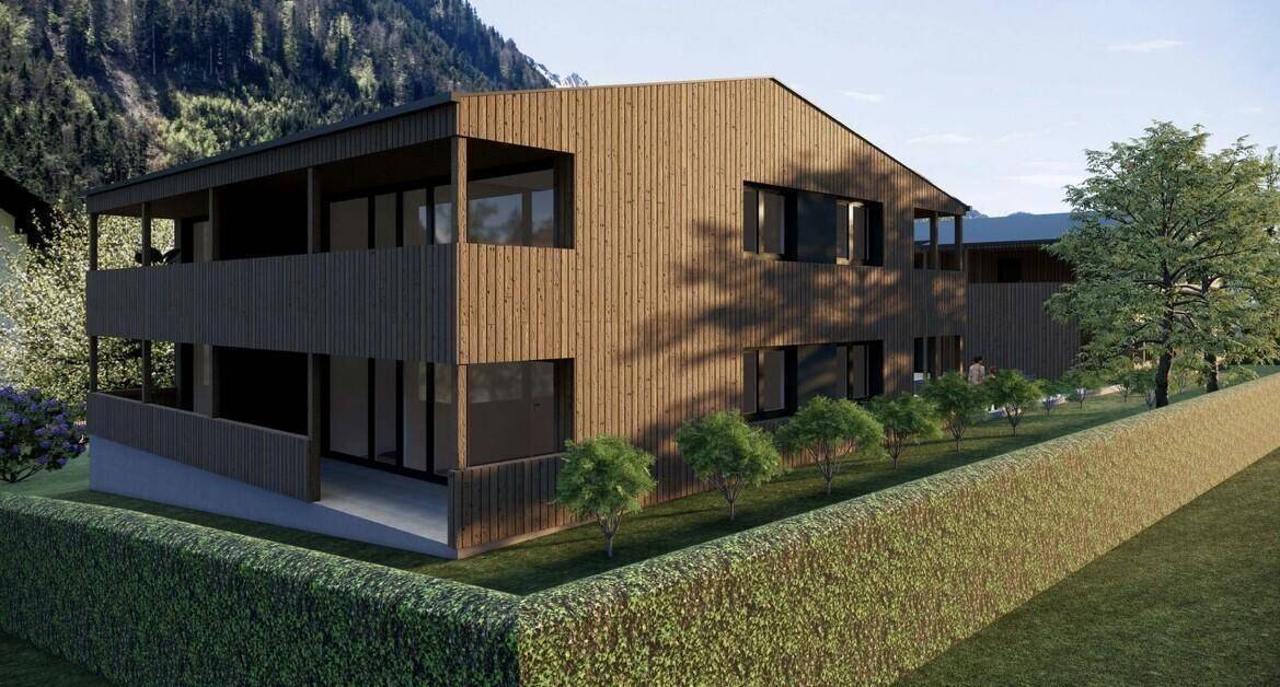 Modernes Gebäude mit Holzverkleidung, Balkonen und gepflegter Hecke im Vordergrund.