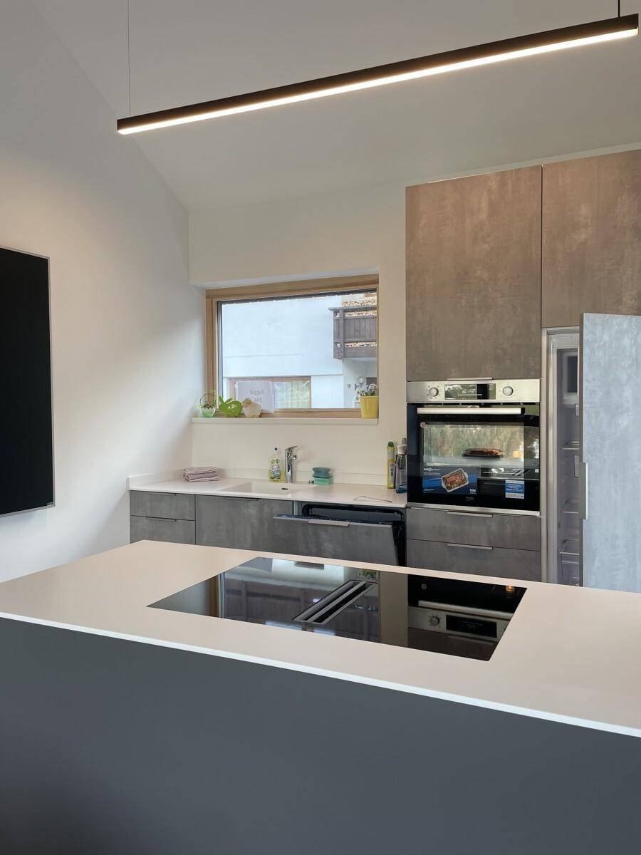 Geräumige moderne Küche mit grauen Fronten, Kochinsel und viel Tageslicht durch das Fenster.
