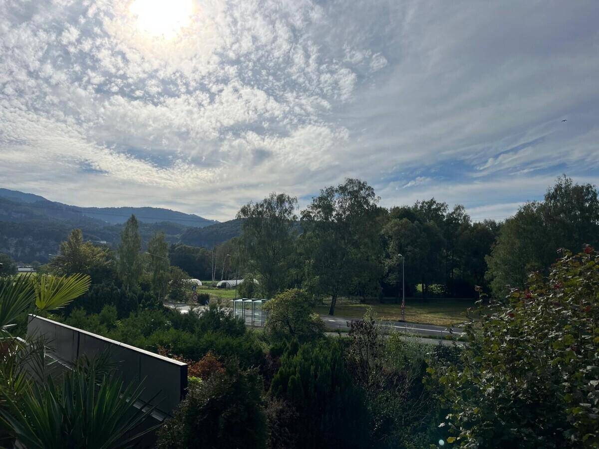 Panoramablick über die grüne Landschaft mit Bergen und bewölktem Himmel, helles Sonnenlicht.