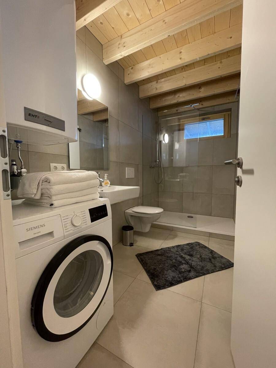 Modernes Badezimmer mit begehbarer Dusche, Waschmaschine und Holzbalkendecke.