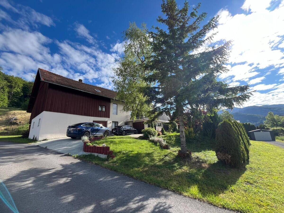 Vorderansicht des Hauses mit geparkten Autos, Bäumen und weitem Blick auf die umliegende Berglandschaft.