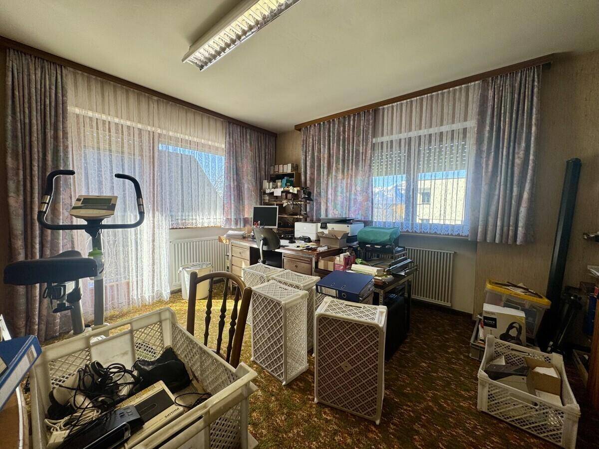 Arbeitszimmer mit Schreibtisch, Bürostuhl und einem Heimtrainer, mit Teppichboden.