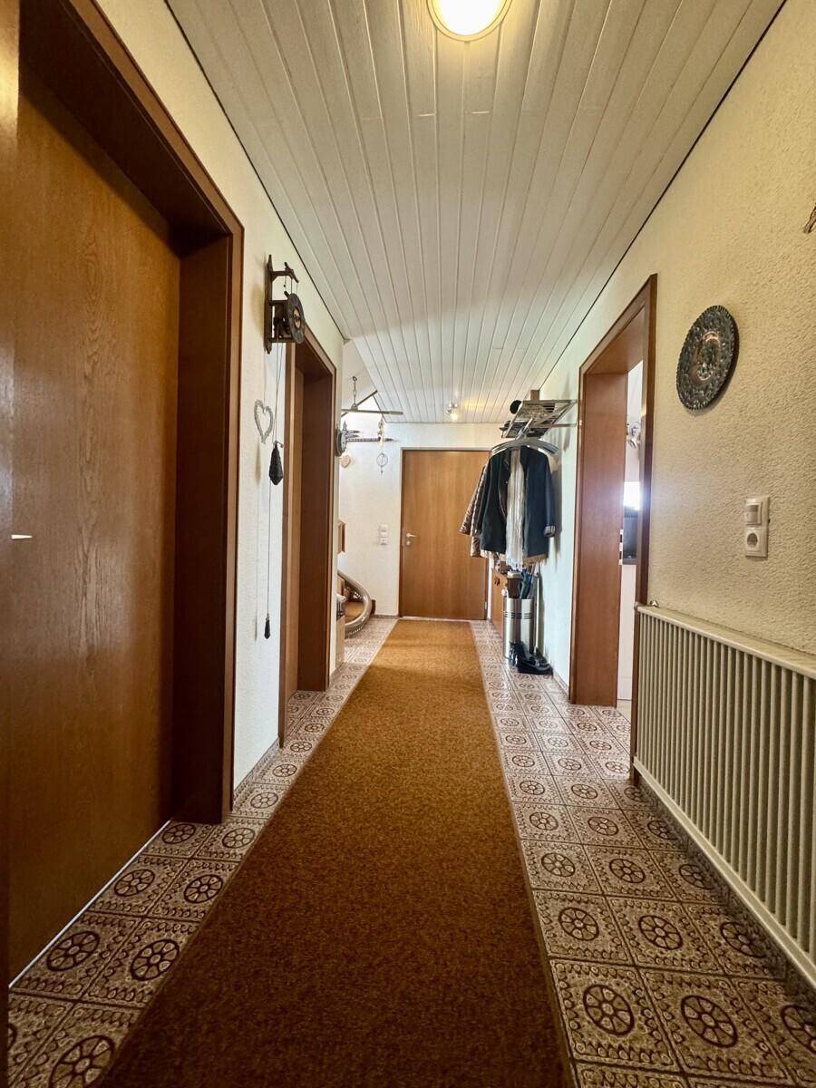 Langer Flur mit gemusterten Bodenfliesen, Holzvertäfelung an der Decke und Garderobe.