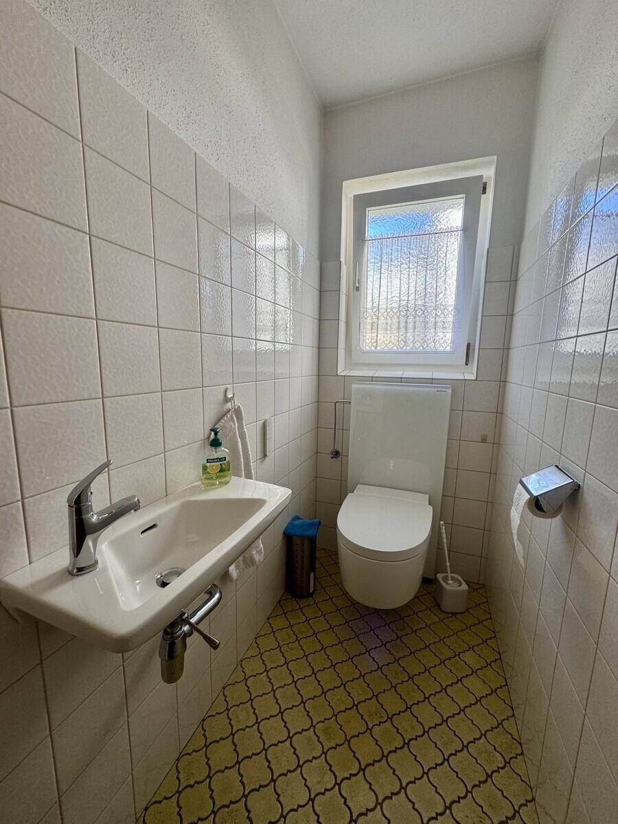 Kleines Gäste-WC mit Fenster, Wandfliesen und gemustertem Boden.