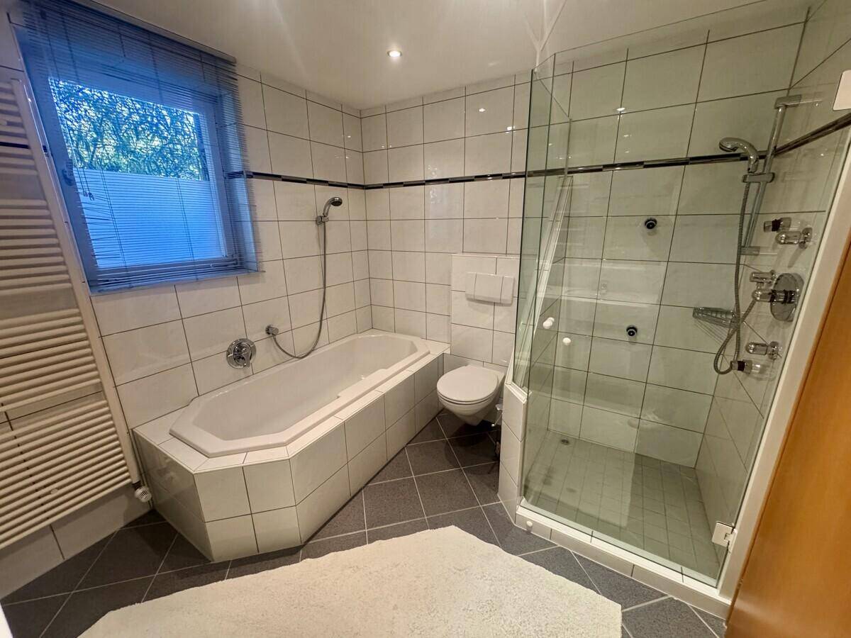 Badezimmer mit Badewanne, separater Duschkabine und Fenster für natürliche Belüftung.