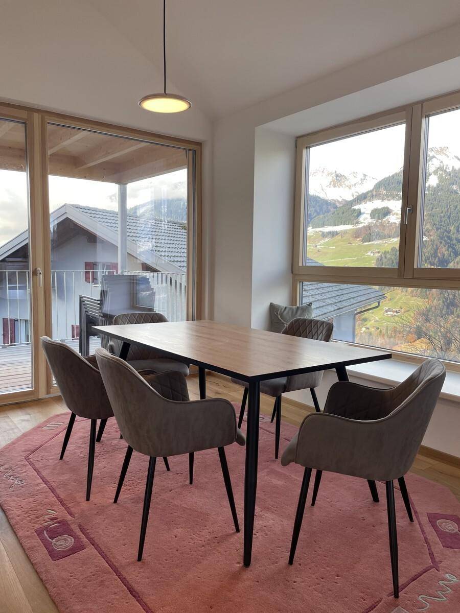 Heller Essbereich mit Holztisch, modernen Stühlen und weitem Blick auf die Berge und den Balkon.