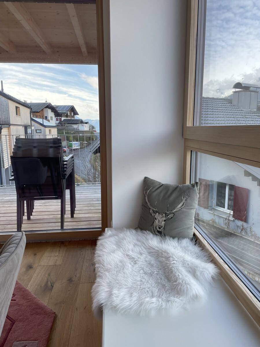 Gemütlicher Fenstersitzplatz mit Kissen und Blick auf den Balkon und die umliegenden Häuser.