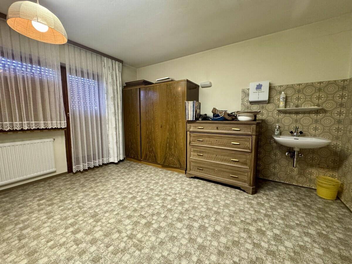 Schlafzimmer mit Teppichboden, Holzschrank und einem kleinen Waschbecken.