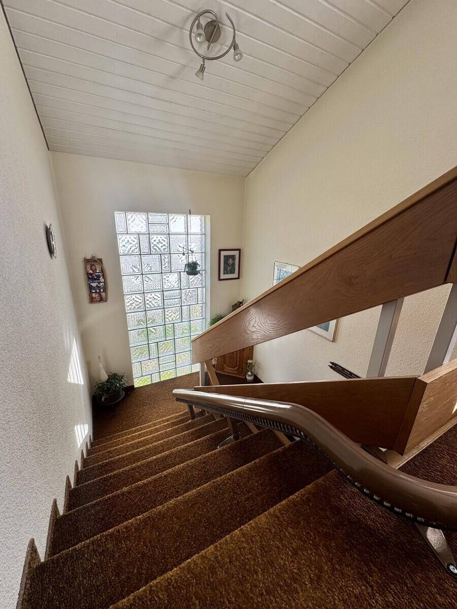 Treppenhaus mit Holzgeländer und einem großen Glasbausteinfenster für natürliches Licht.