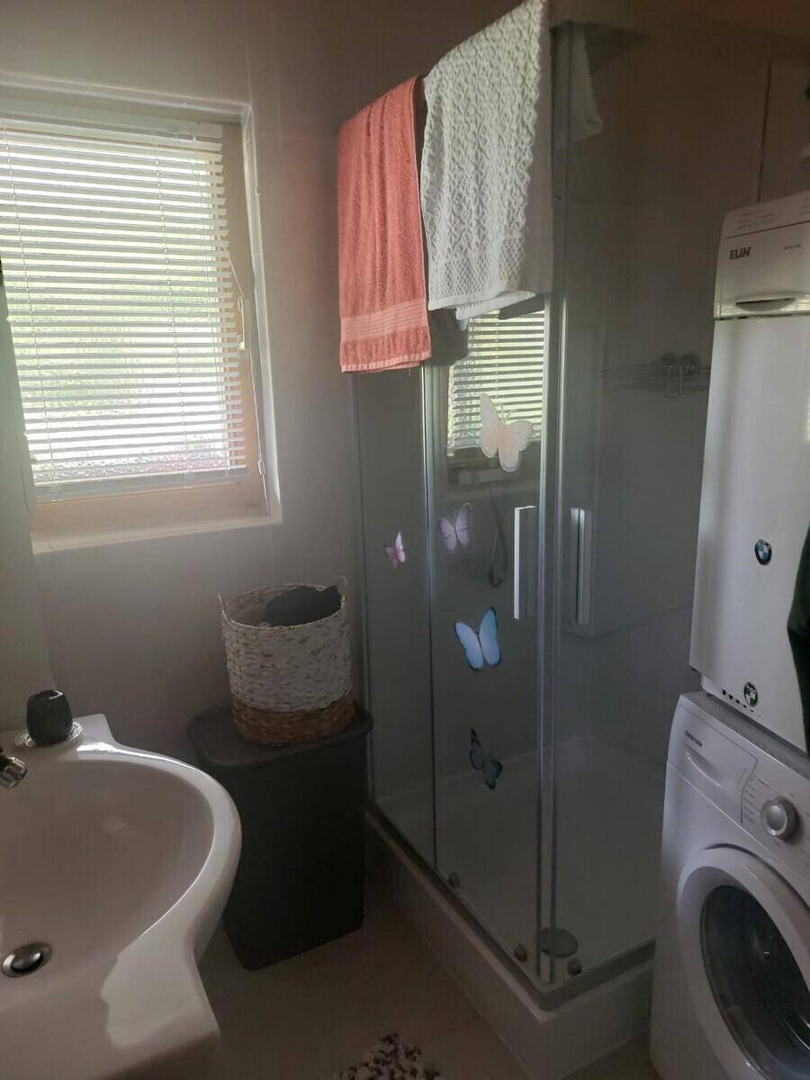 Badezimmer mit Duschkabine, Waschbecken, Waschmaschine und einem Fenster mit Jalousien.