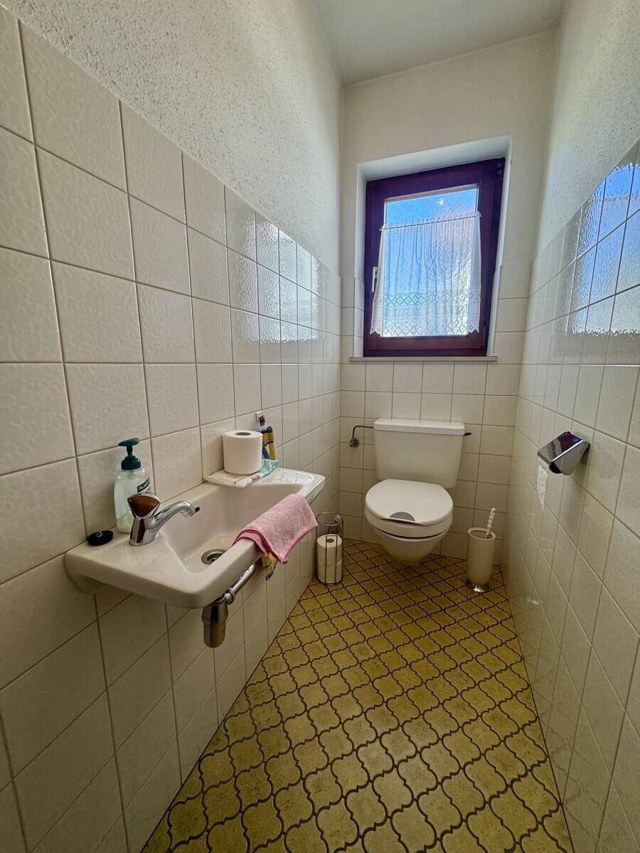 Kleines Gäste-WC mit Fenster, Wandfliesen und gemustertem Boden.