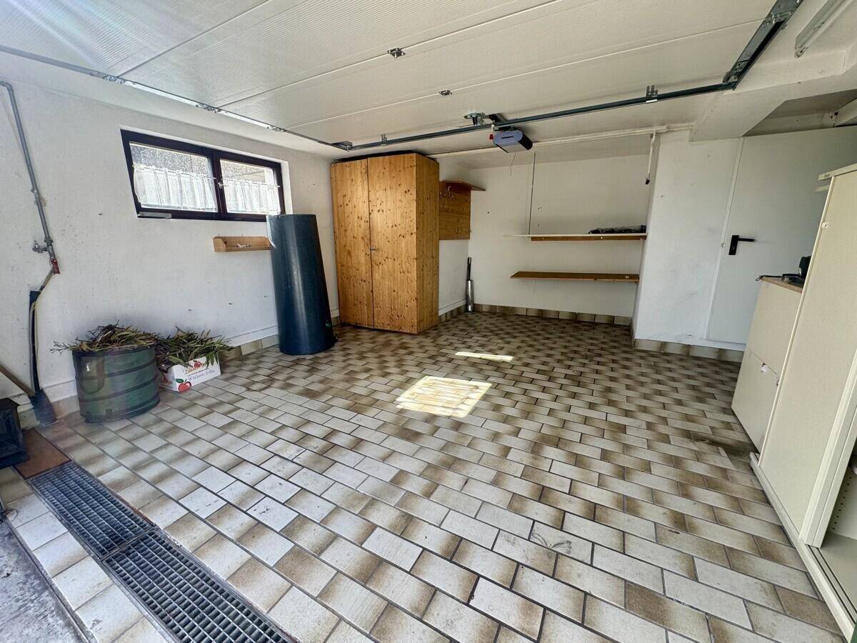 Geräumige Garage mit gefliestem Boden und Fenster, bietet viel Platz für Fahrzeuge und Lagerung.