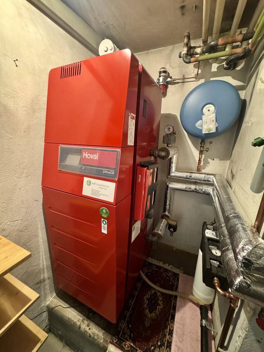 Heizungsraum im Keller mit einem großen roten Heizkessel und Rohrleitungen.