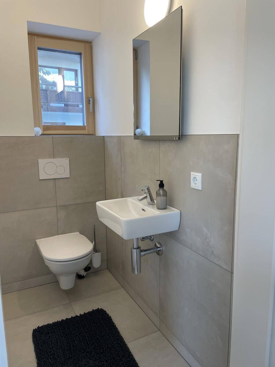 Kleines Gäste-WC mit modernem Design, wandhängender Toilette und Fenster für Tageslicht.