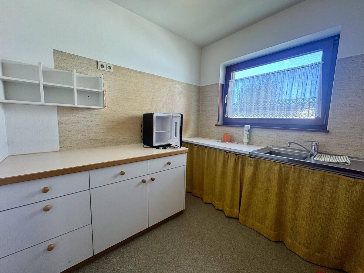 Ältere Küche mit weißen Unterschränken, Spüle und kleinem Kühlschrank, mit Fenster.