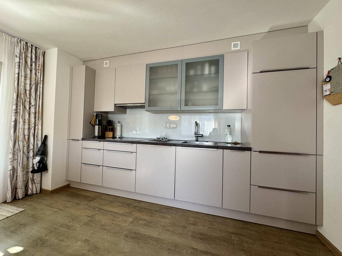 Moderne Küche mit hellgrauen Schränken, integrierten Geräten und Laminatboden.