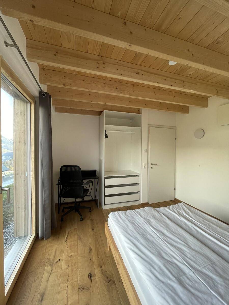 Helles Schlafzimmer mit Holzbalkendecke, Holzboden und großem Fenster mit Ausblick.