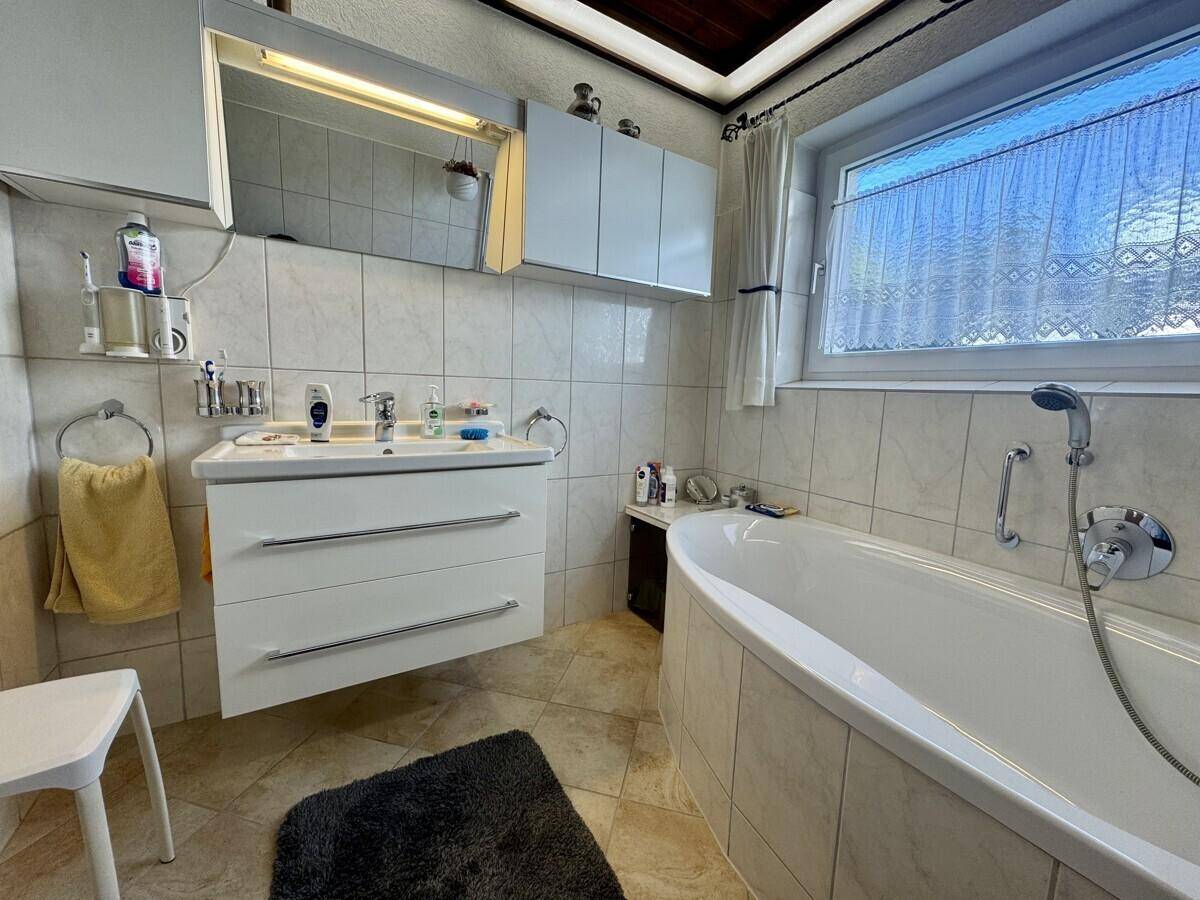 Badezimmer mit Badewanne, Waschtisch und Spiegelschrank, hell gefliest.