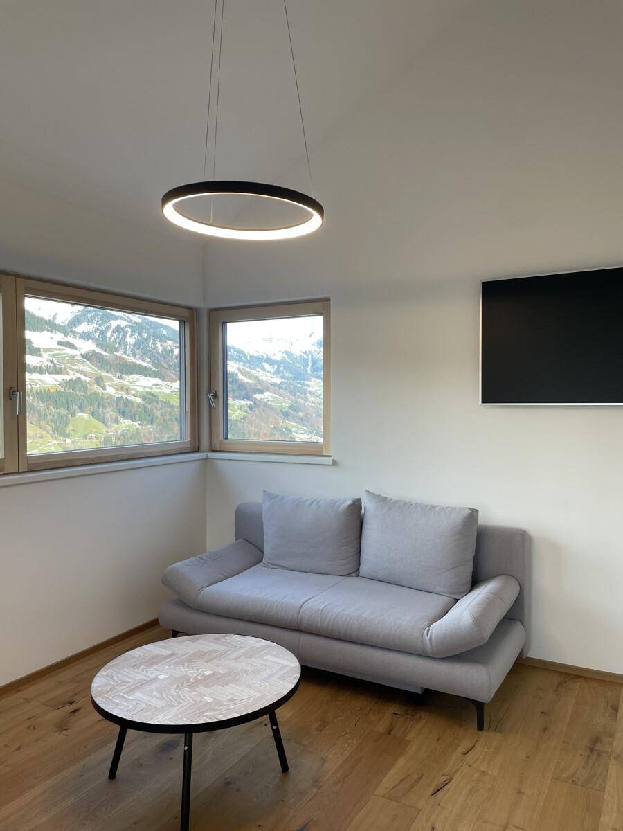 Gemütliches Wohnzimmer mit grauem Sofa, Couchtisch und Panoramablick auf die Berge.