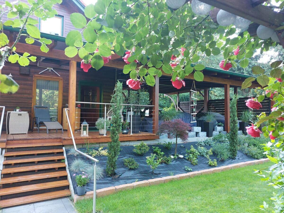 Holzterrasse mit Treppe und bepflanzten Gartenbeeten, umgeben von Rosen und üppigem Grün.