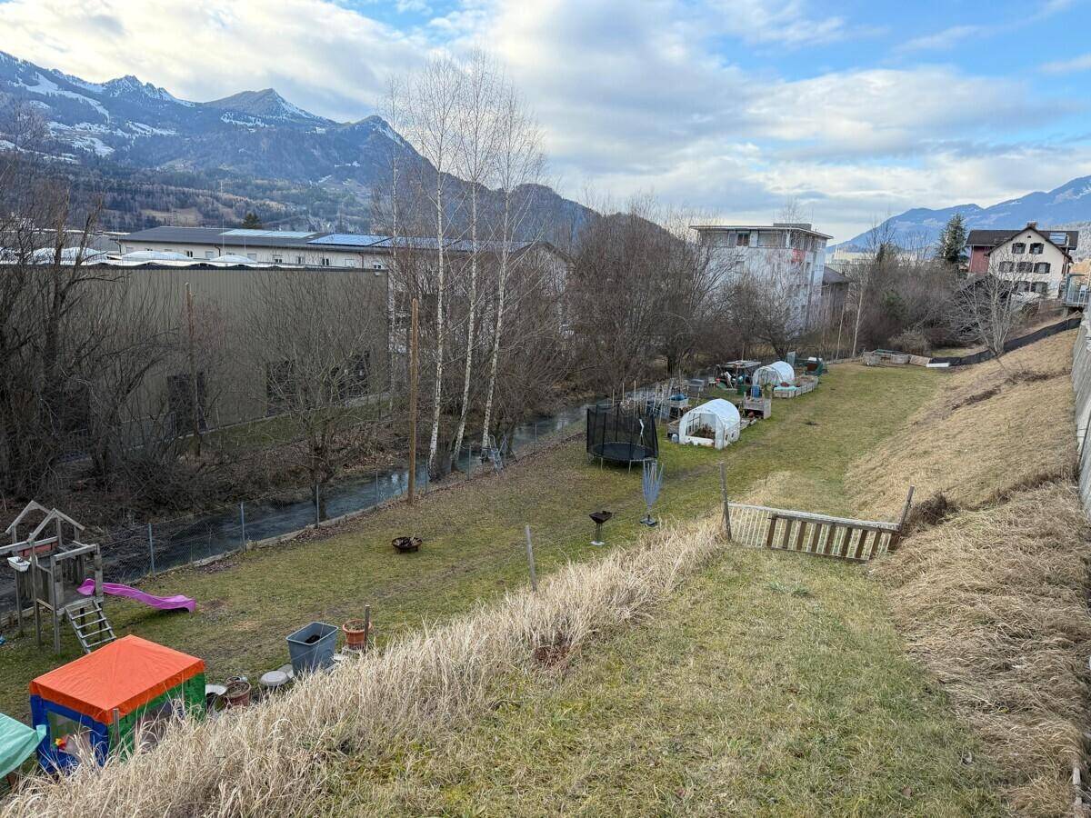 Weitläufiger Gartenbereich mit Spielgeräten, Trampolin und Blick auf die umliegende Berglandschaft.
