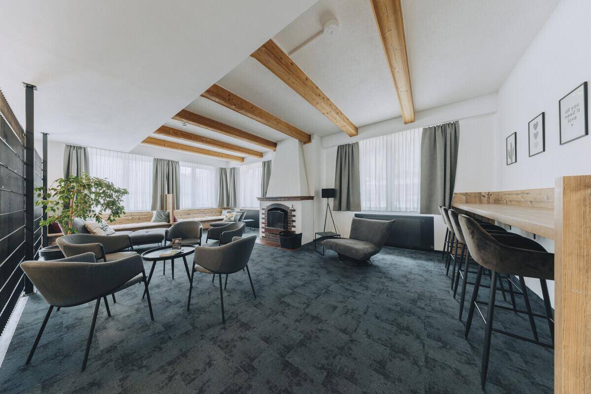 Gemütlicher Loungebereich mit sichtbaren Holzbalken, einem Kamin und verschiedenen Sitzgelegenheiten, ideal zum Entspannen.