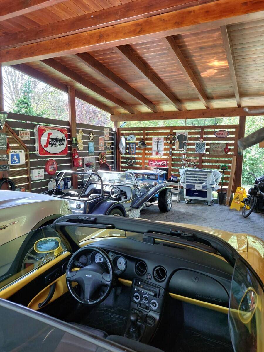 Geräumiger Holzcarport mit mehreren Fahrzeugen und Werkzeugen, dekoriert mit Vintage-Schildern.
